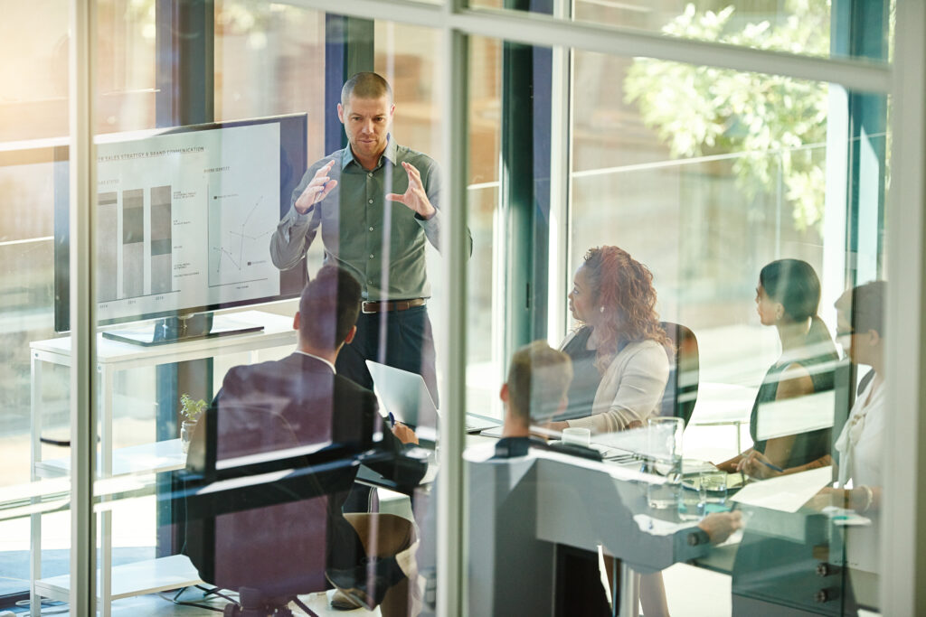 Business people, tech or advice in boardroom for training, productivity report or feedback chart on screen. Speaker, team or corporate presentation in office for company growth with brand management A speaker presents a productivity report to a focused team in a modern boardroom.