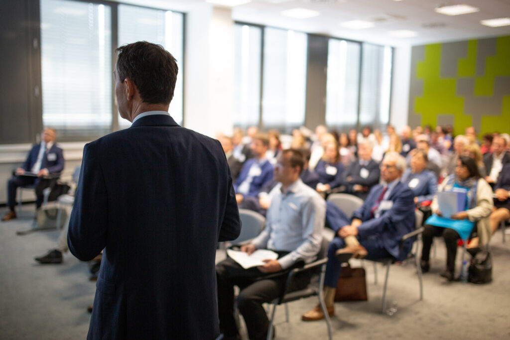 conference, meeting of business stategy A speaker presents to an audience at a business strategy conference. Attendees listen attentively.