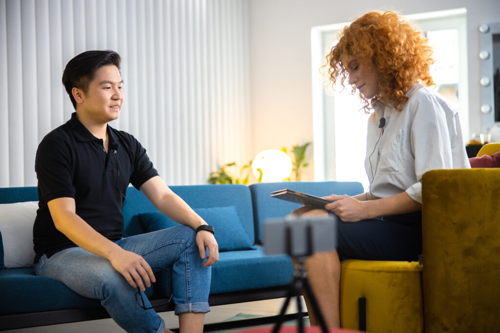 Relaxed man and woman communicating being recorded stock photo Man and woman engage in a video interview, seated in a modern office setting.