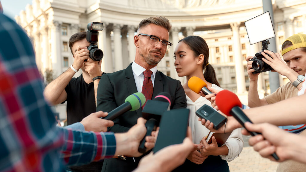 Have you ever wished you were better informed? Journalists conducting interview of politician. Journalism industry, live streaming concept. Politician stands with assistant, surrounded by reporters holding microphones and cameras during an interview.