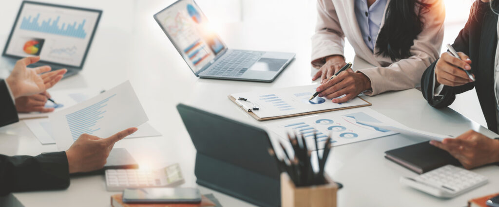 Diverse coworkers collaborate in a boardroom, discussing and analyzing business strategies with documents and laptops.