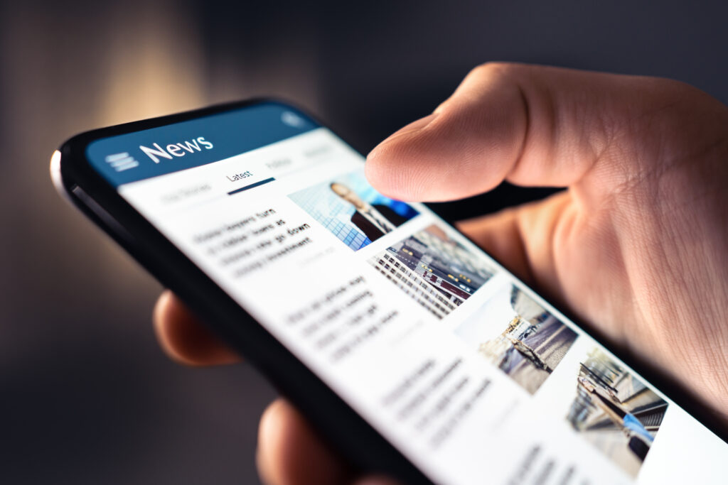 A hand interacts with a smartphone displaying a news app with various article headlines.