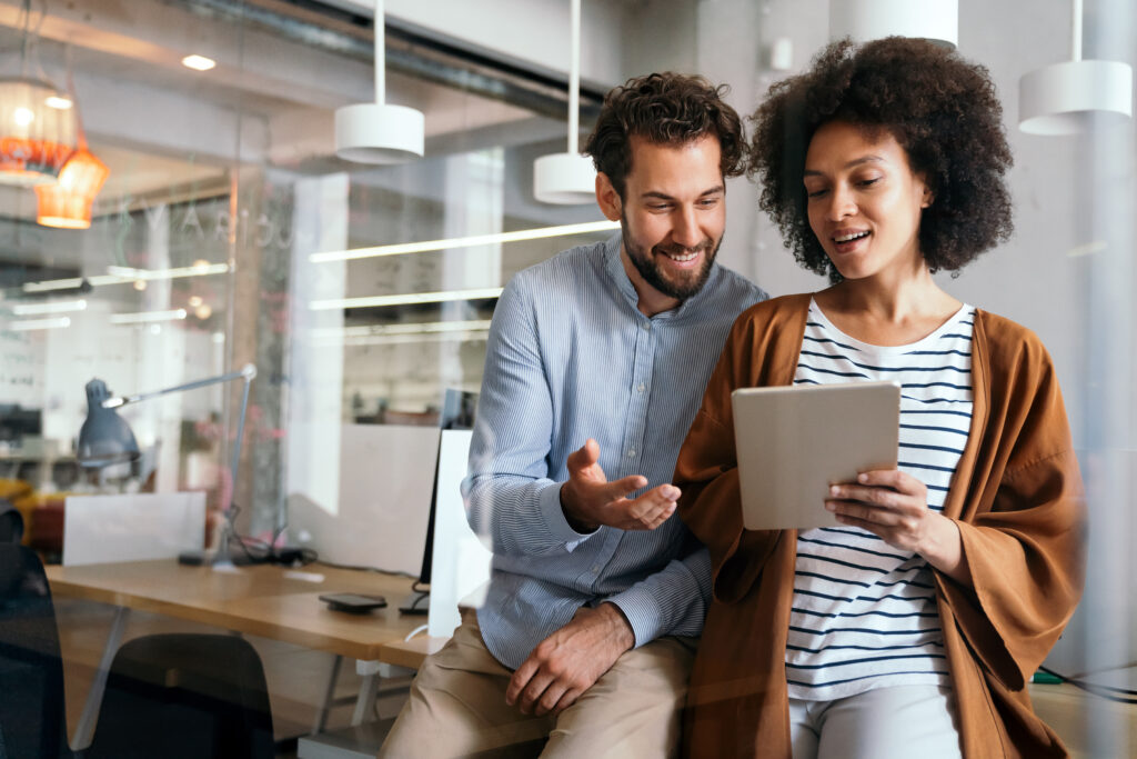 Group of designers, business people at work in corporate office. Startup, happy teamwork concept. Two colleagues discuss a project while reviewing a tablet in a bright corporate office.